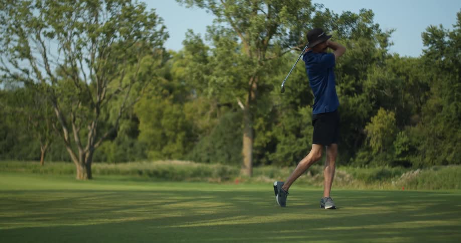 A man playing golf with trees the sky and clouds in the background