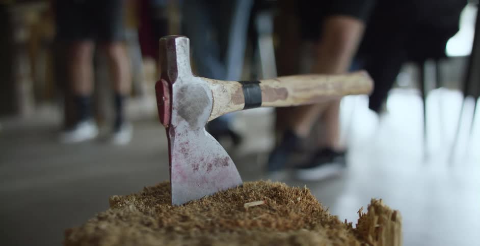 People stand in an open room where an ax sits in a wood trunk