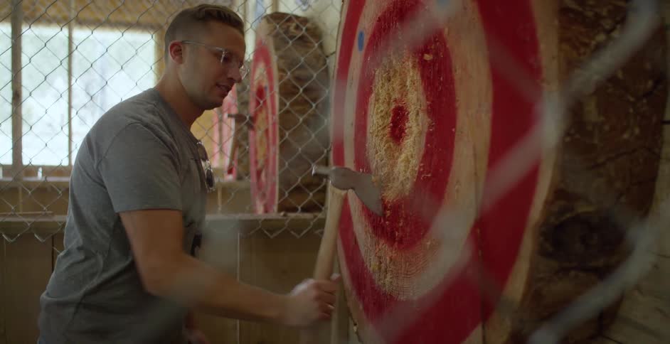 A man in a room taking an ax from a bullseye with a wall and window in the background