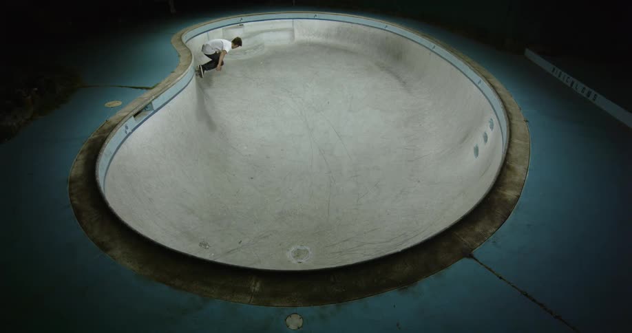 A man with a skateboard skating in an empty swimming pool