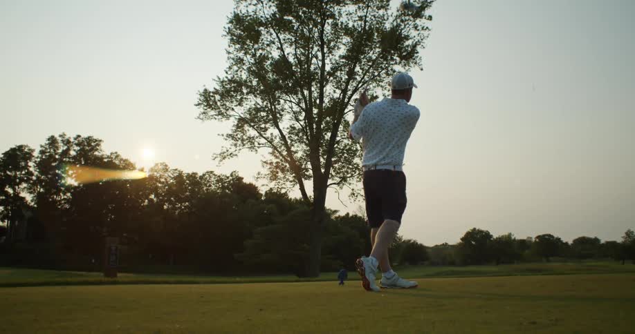 Golfer swing and hits ball down golfing green