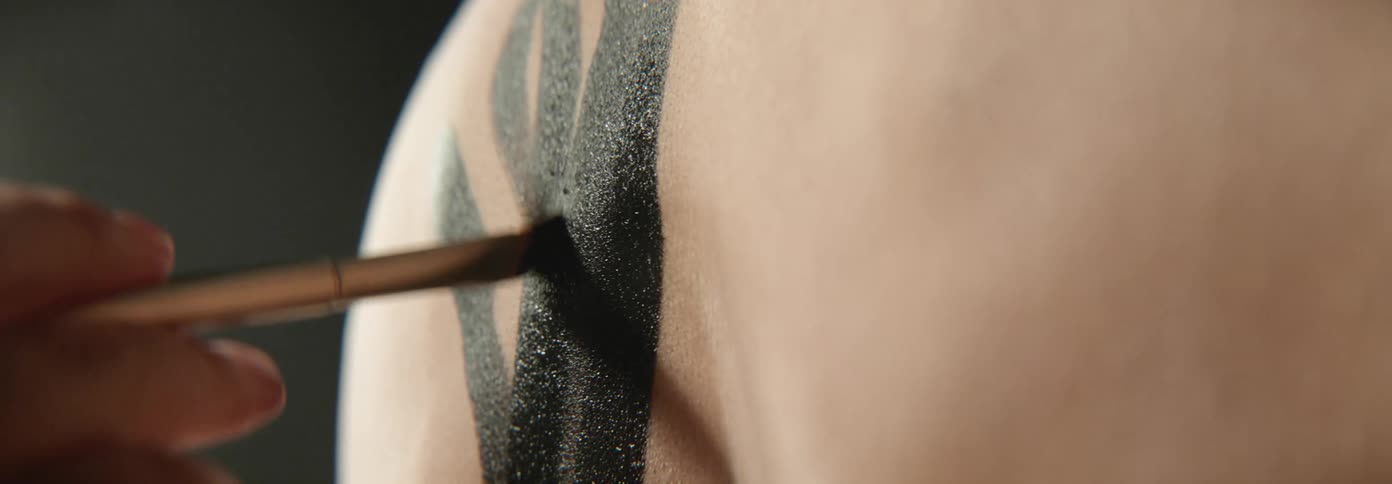 Artists hand paints the back of man with brush