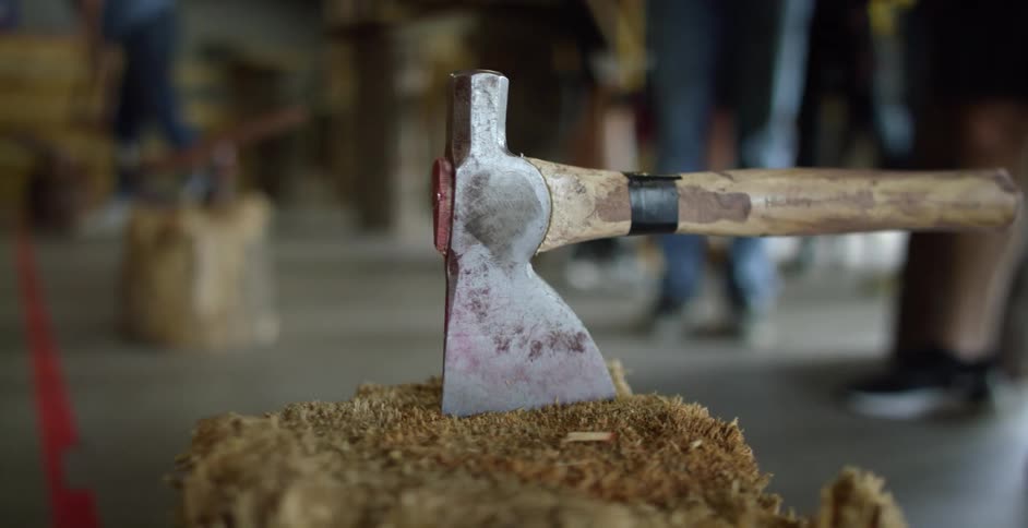 An ax on a piece of wood with people in the background