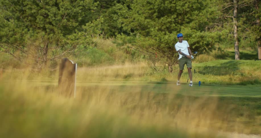 Man with blue cap white shirt and green short plays golf