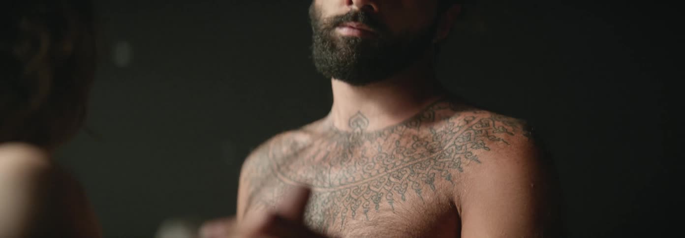 A shirtless man with tattoos paints on a person as someone paints his back in a chain of performance art