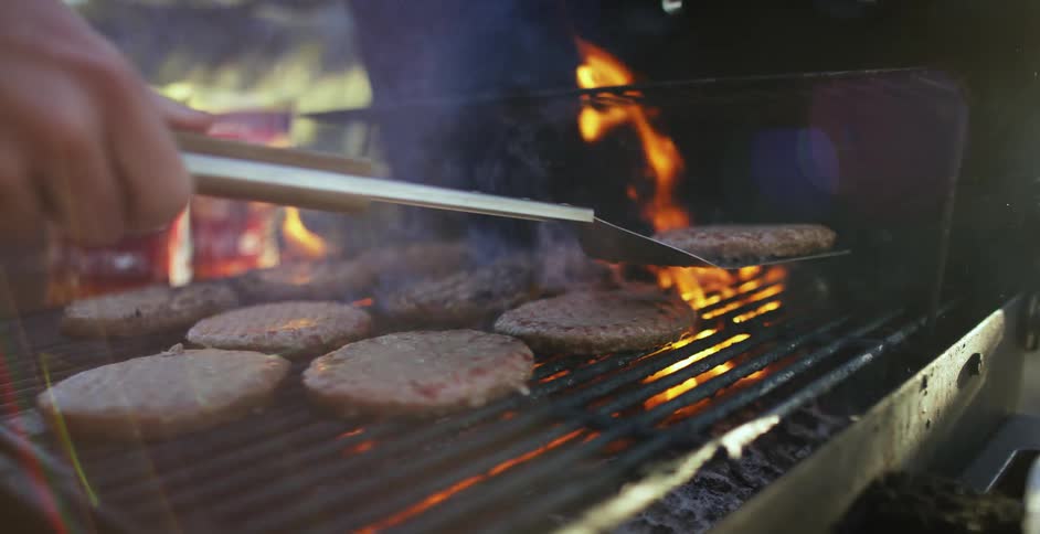 Hamburg patties are flipped over on the barbecue as flames shoot up around them