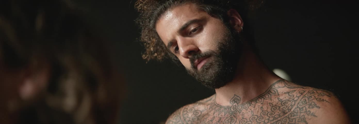 Bearded shirtless tattooed man painting the back of the man in front of him