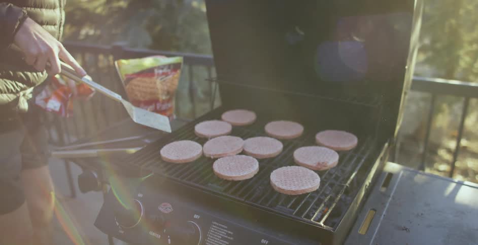 Person wearing shorts grills burger patties on grill on balcony near rail