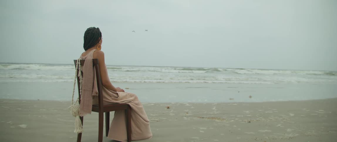Woman wearing a pink dress sitting on a chair over the sand on a beach next to the ocean