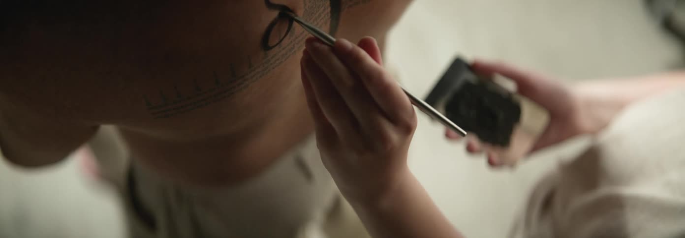 Artist painting the bare back of a person with black henna ink using a small brush