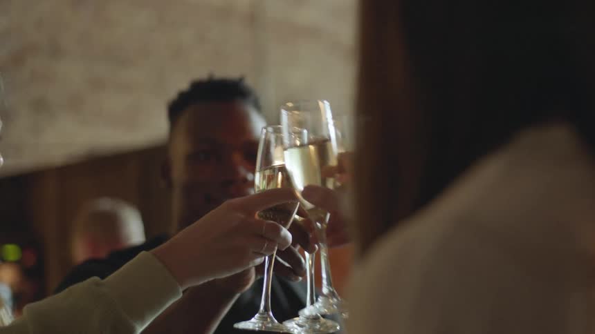 A group of young people cheers their champagne classes together in a restaurant