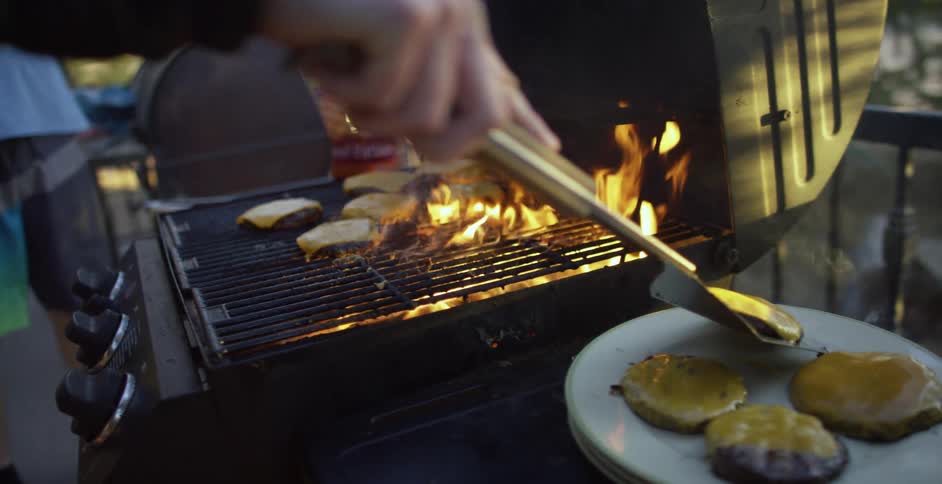 A person uses a spatula to lift a cheeseburger off a grill and place it on a plate