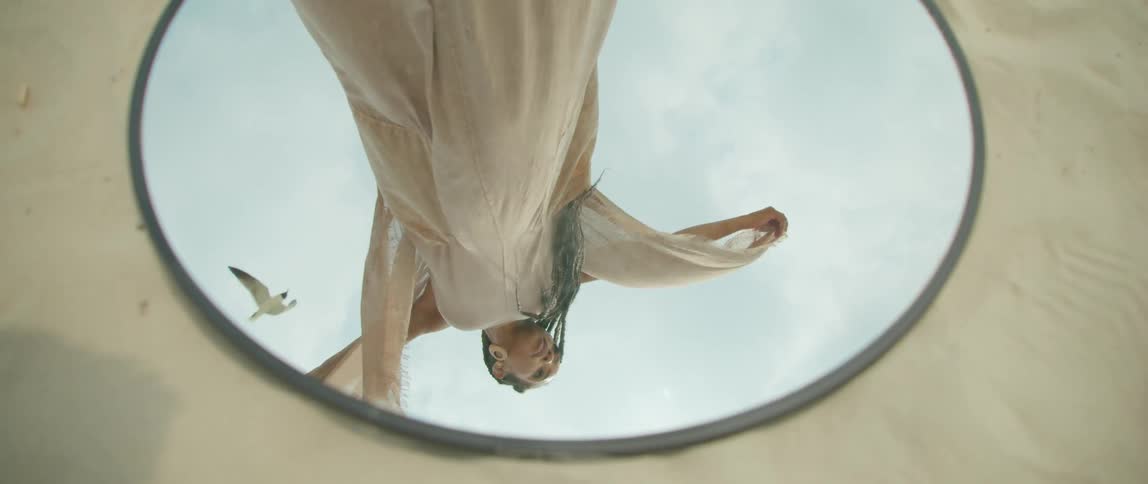 Reflection on a mirror over the sand of a woman wearing a dress waving in the wind