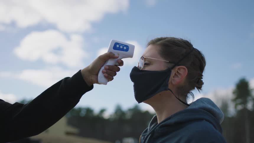 Woman wearing a face mask gets temperature measured before entering the workplace