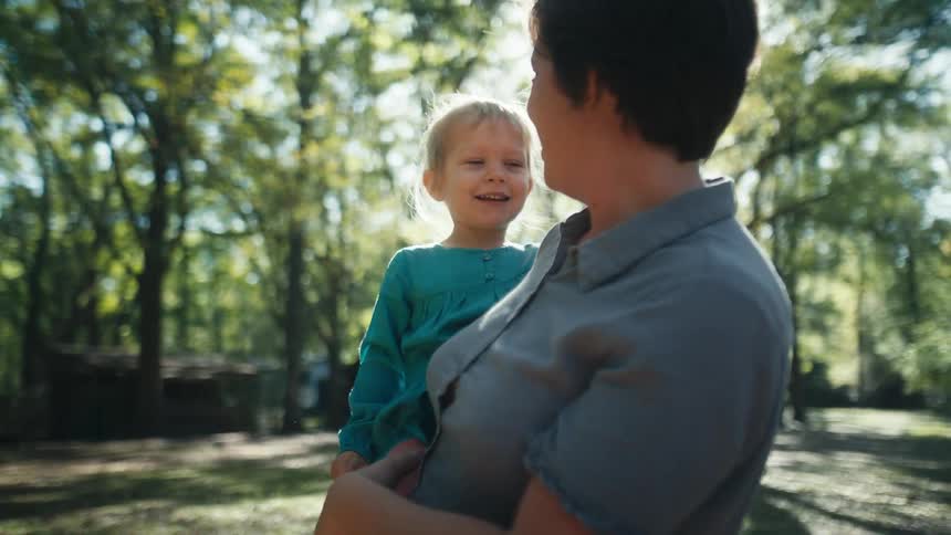 A mother holding her young blonde toddler outside on a sunny summer day