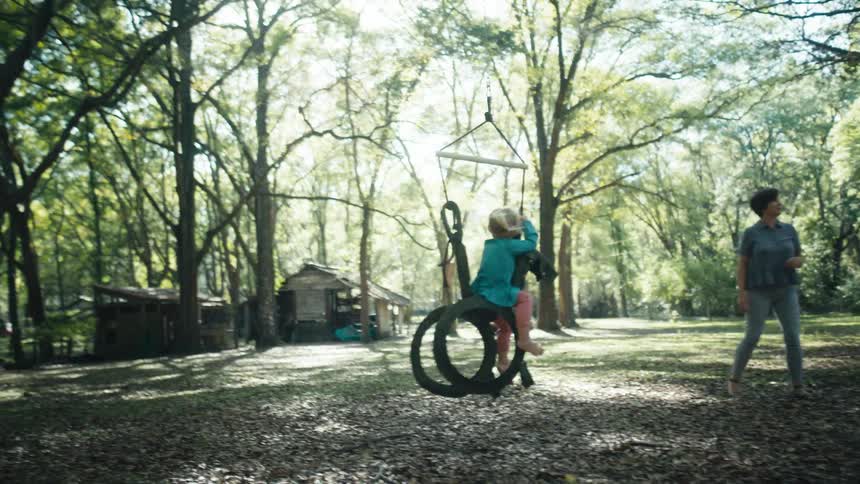 A young girl swings on tree swing as a woman watches her from nearby