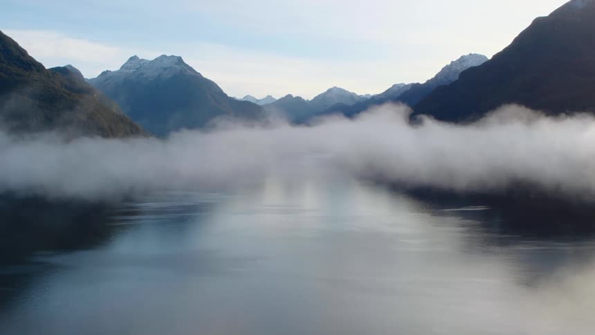 Fog moves over a lake between mountains under a cloud filled sky