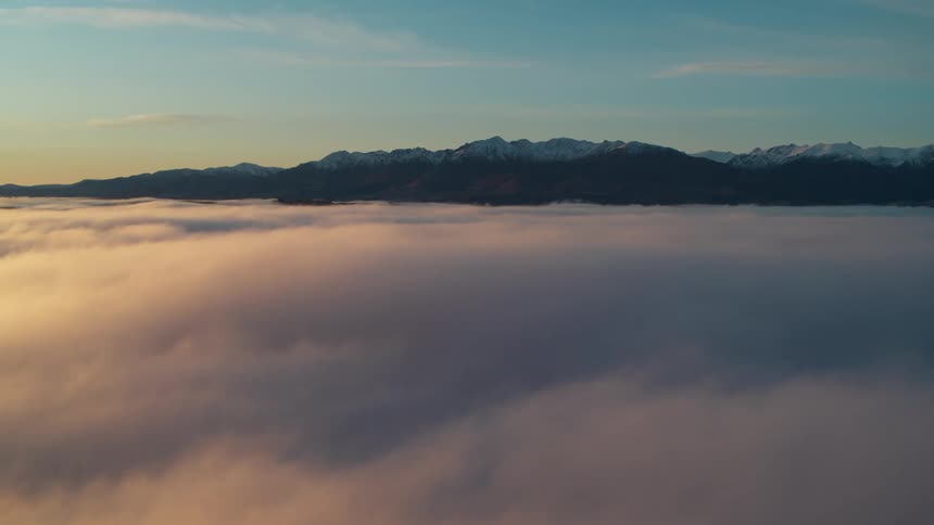 Snow capped mountains loom behind a sea of clouds during the day