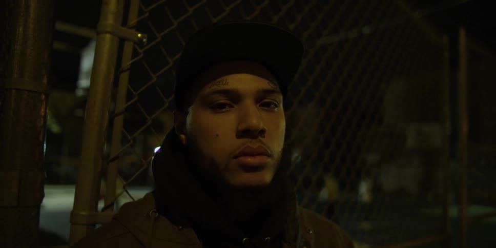 A man stares forward leaning against a fence at night