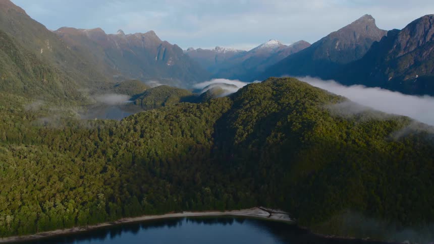 Mountain valley filled with fog and a lake with a mountain range in the distance