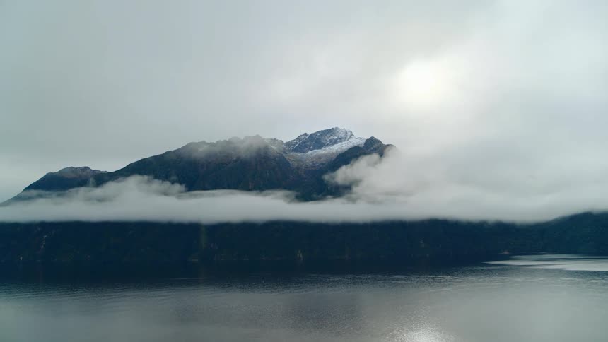 A layer of fog hovering around a snowy mountain by a lake