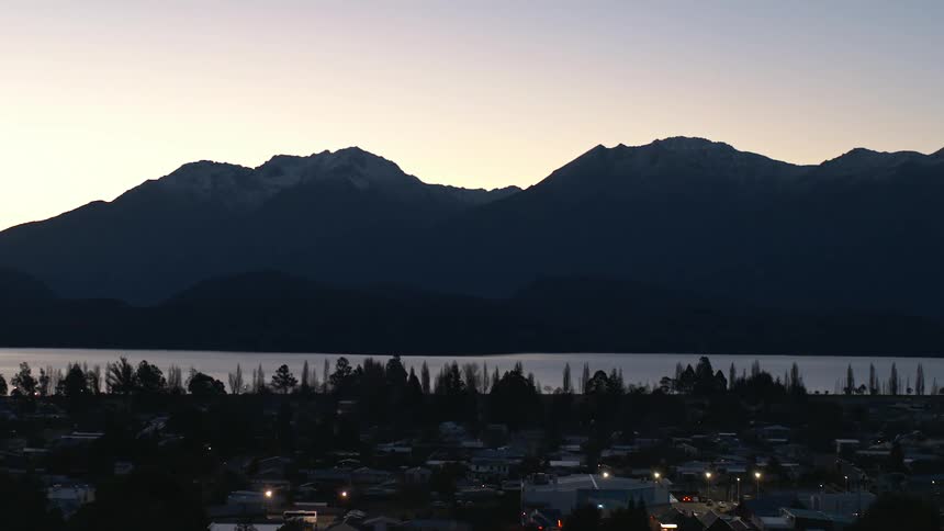 A mountain looms over a lake and the town on the lakeshore at sunset