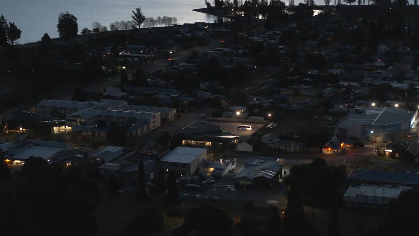 Building lights brighten dark neighborhood sitting on slight slope as traffic drives along street