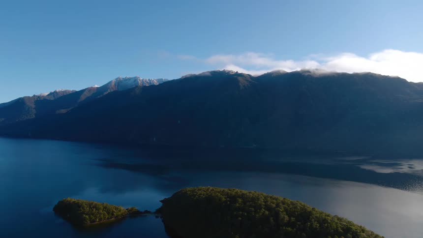 Mountain range alongside a lake and a few clouds in the sky
