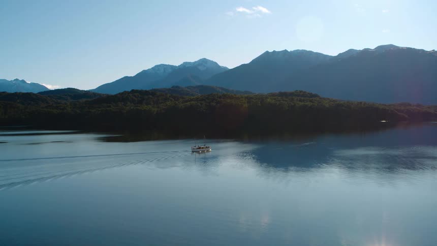 A boat slowly makes its way across a body of water with mountains in the background
