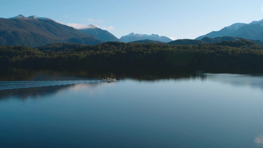 A boat leaves a wake in the smooth surface of the lake which reflects the trees and sky