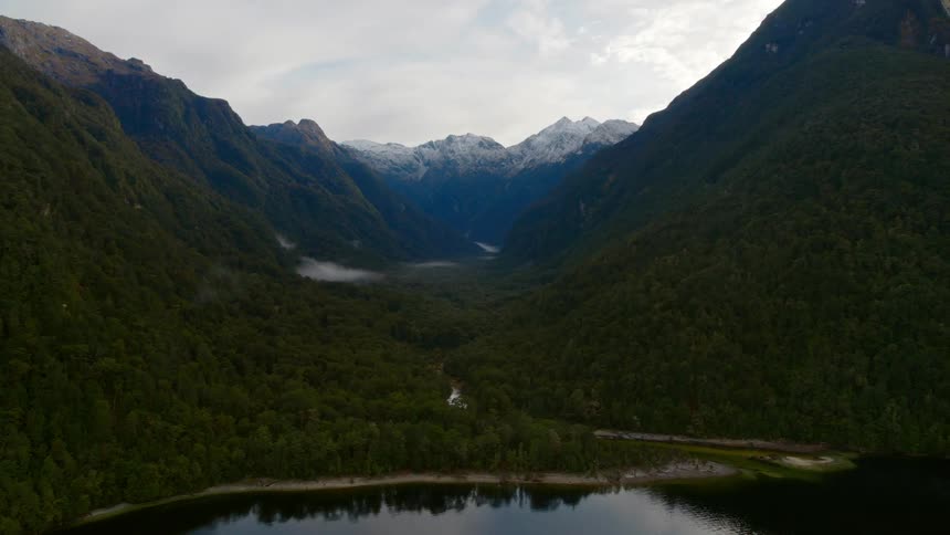 A river in a valley surrounded by trees with a mountain range the sky and clouds in the background