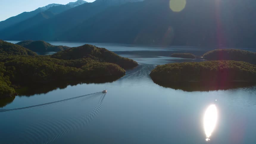 A boat travels on a calm lake during the day with mountains in the background