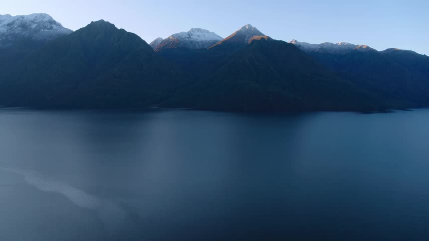 A lake with a mountain range with snow with the sky and clouds in the background
