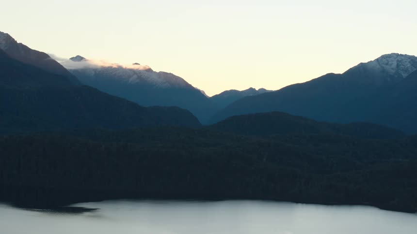 Fog above a lake between mountains with more mountains in the distance