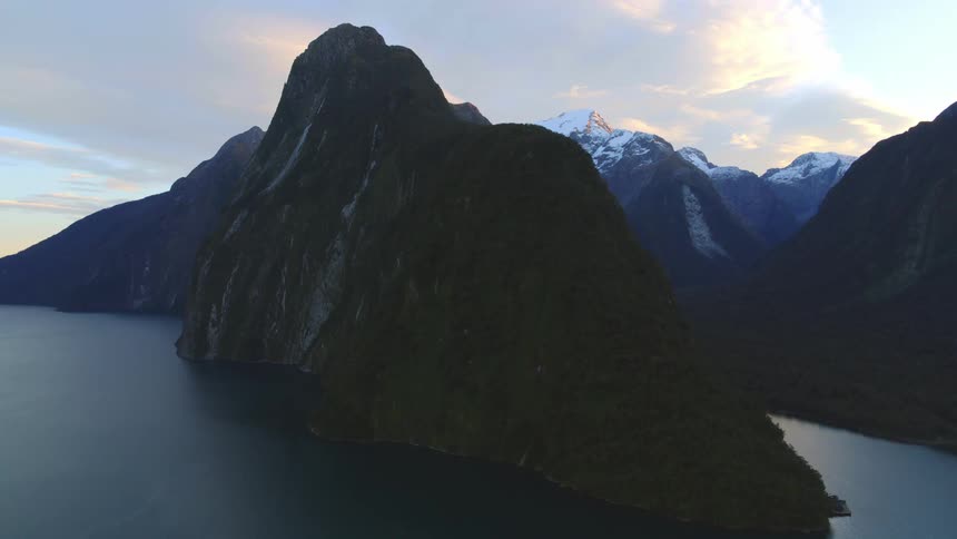 Rock formation in a lake and snow covered mountains in the distance under a cloudy sky