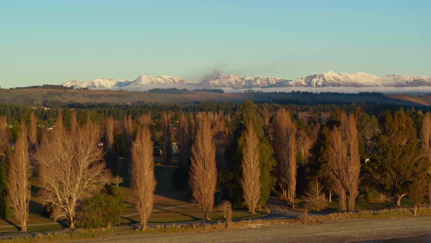 Lake with trees along the coastline and snow covered mountains in the distance