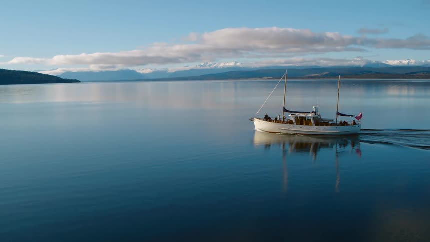 Aerial view of a small fishing boat driving over the calm surface of a lake near the mountains