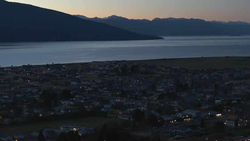 A town with houses roads and trees with a lake a mountain range the sky and clouds in the background