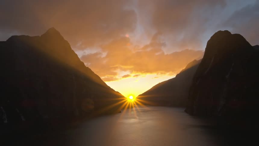 Sun rises and moves through gap at end of lake between mountains under a red sky