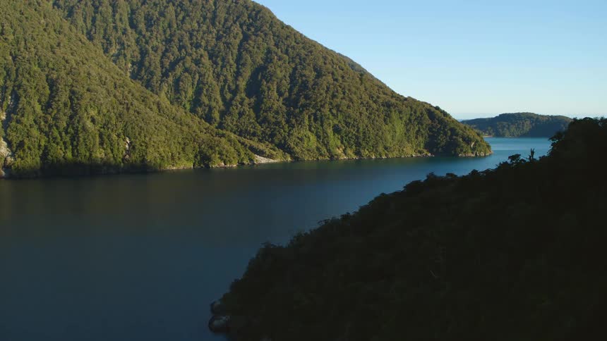 An aerial view of an ocean inlet with hilly forests and the horizon in the background