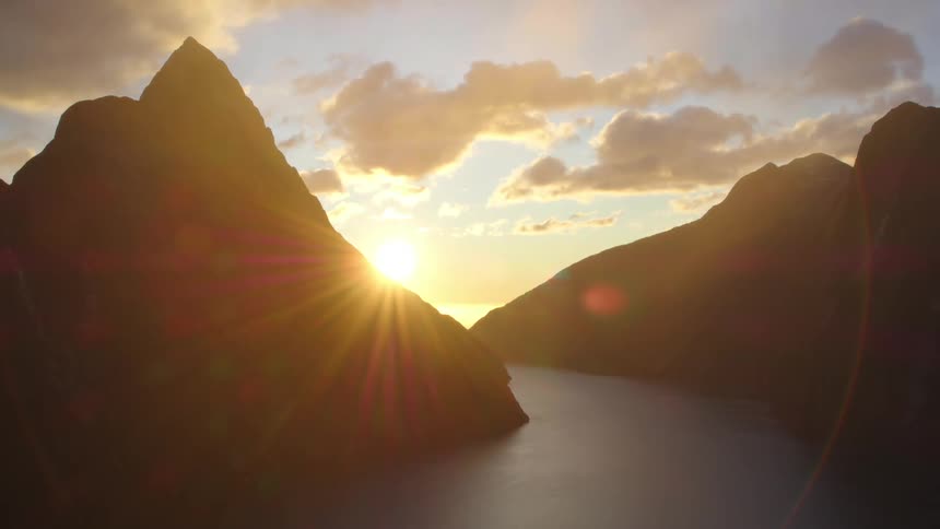 Sunlight shining behind mountains at a fjord opening to the sea at dusk