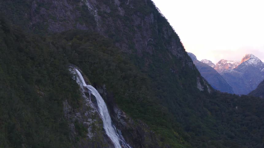 Aerial view of a waterfall flowing off the side of a mountain on a mountain range at morning