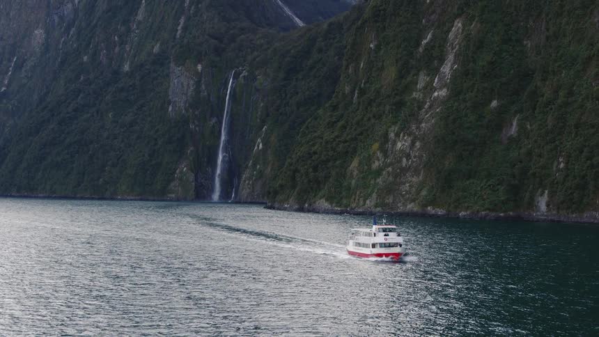 A large boat travels along the mountainous coast of a landmass during the day