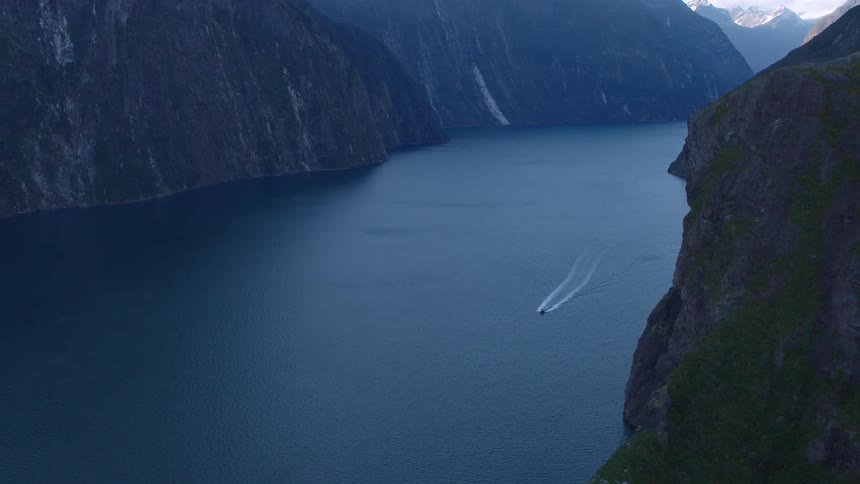 A boat is traveling through a fjord surrounded by steep mountains