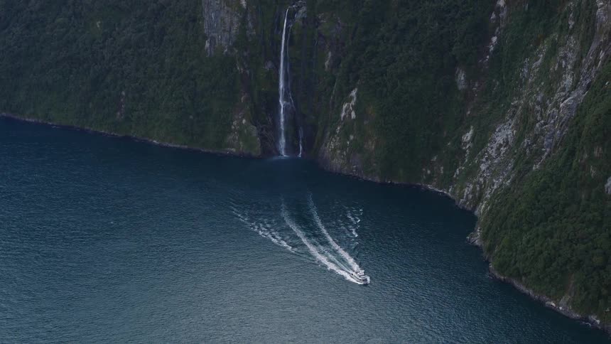 A boat glides through the water near a tall cliff with a waterfall
