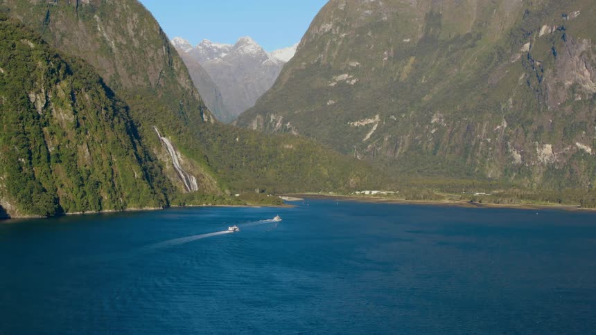 Boats move through the lake water towards a mountain coastal area