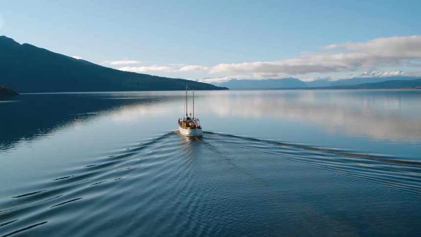An aerial view of a boat sailing on a calm mountain lake on a sunny day