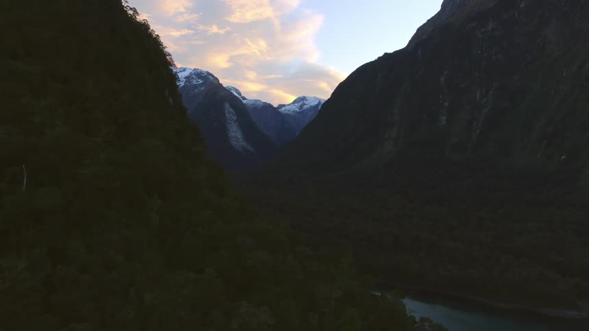 Aerial view of a rover flowing between the peaks of a mountain range at sunset