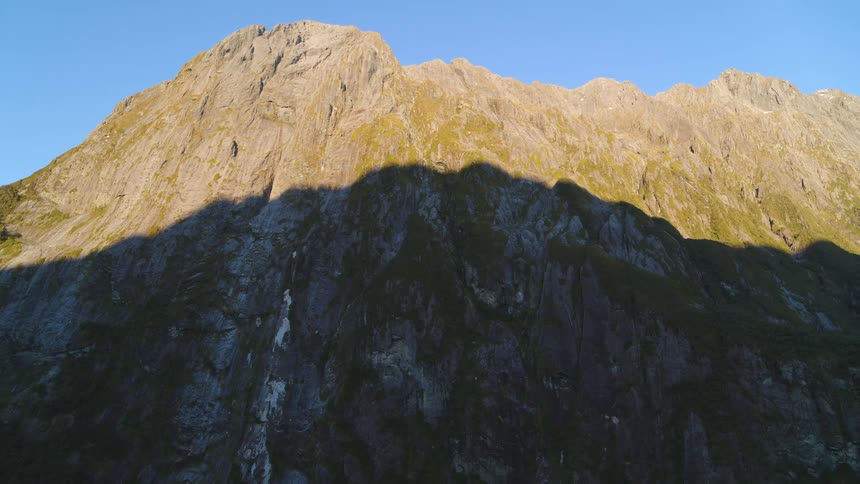 A rock mountain ridge covered in patches of vegetation under a clear blue sky
