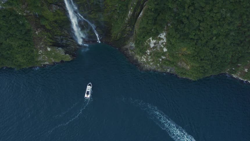 A large boat sails away from a waterfall on the coast as another boat approaches the waterfall